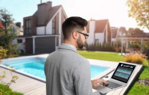 Man next to a backyard pool using pool automation app on his laptop.
