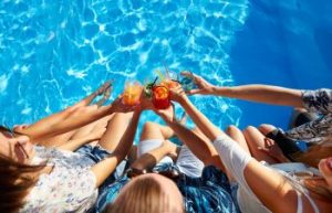 Group of friends with colorful coctails by a backyard swimming pool.
