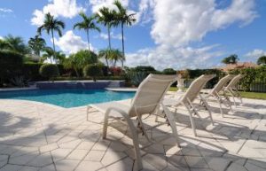 Outdoor swimming pool with paver patio and poolside furniture on it.