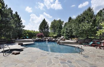 Backyard swimming pool with large flagstone patio and water features.