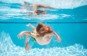 Young boy diving and swimming under water in a pool.