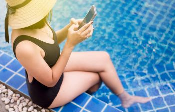 Woman using pool automation app sitting on the edge of bakyard pool.