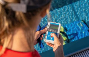 A woman standing at a swimming pool and using a remote controller for pool automation system